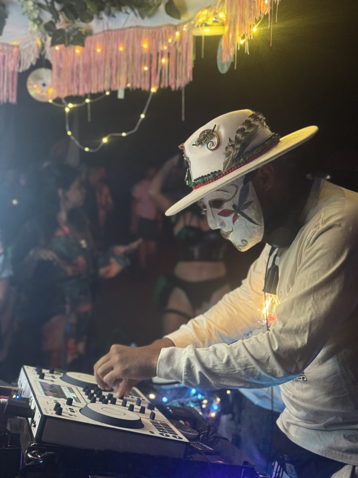DJ in a skull mask wearing a white feathered fedora