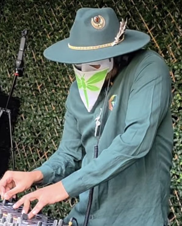 Person wearing green fedora and mask at an outdoor event